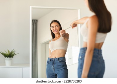 I choose myself. Playful young lady pointing finger at her reflection in mirror, enjoying successful slimming, free space. Self confidence concept
