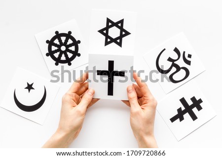 Choose religion concept. Hand with catholic cross near world religions symbols on white background top view