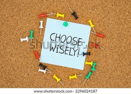 Choose wisely text on light blue post-it paper pinned on bulletin cork board surrounding by multi color pins. This message can be used in business concept about choosing.