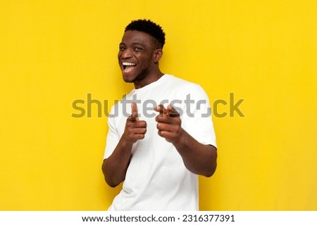 I choose you. happy african american man in white t-shirt points with his hands at camera on yellow isolated background, toothy guy laughs and chooses you