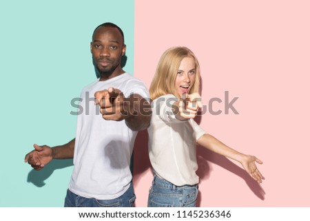 I choose you and order. The smiling mixed couple point you, want you, half length closeup portrait on studio background. The human emotions, facial expression concept. Front view. Trendy colors