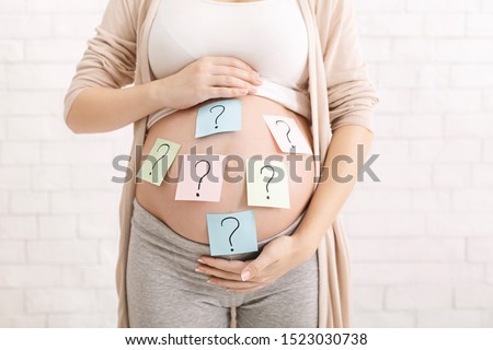 Choosing baby name. Confused pregnant woman with question marks on paper stickers on tummy