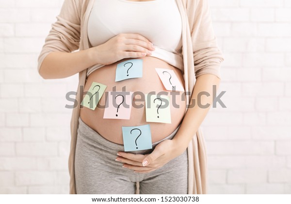 Choosing baby name. Confused pregnant
woman with question marks on paper stickers on
tummy