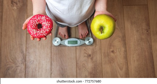 Choosing between donut and apple. Man with donut and apple in his hands measuring body weight on scales. Healthy diet or junk sweet food. 
