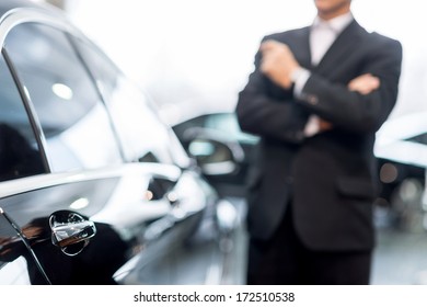 Choosing a car at dealership. Thoughtful grey hair man in formalwear leaning at the car and looking away