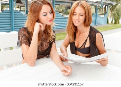 Choosing Cocktail. Two Pretty Young Girlfriends Sitting In Cafe And Looking Through Price List