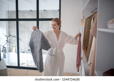 Choosing Favorite Sweater. Blonde Young Woman Smiling While Choosing Favorite Sweater In The Morning