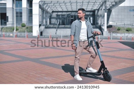 Choosing a path. A young and stylish man gazes thoughtfully into the distance, pausing during his ride on an electric scooter through the sunny city in the summer