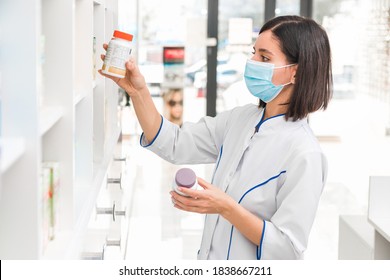 Choosing The Right Medicine. Professional Looking Female Pharmacist With Medical Mask On In Drug Store Studying The Prospectus Of A New Drug