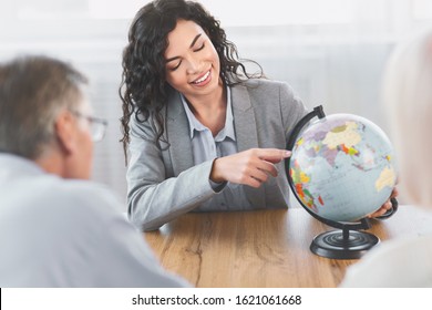 Choosing Trip. Beautiful Mexican Agent Proposing Last Minute Travel Offer To Mature Couple, Pointing At Globe, Copyspace