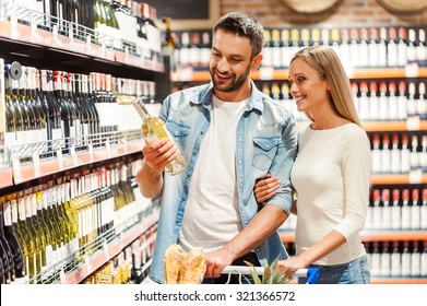 Choosing wine for dinner. Happy young couple choosing wine together while standing in wine store 