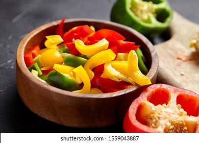 Chopped bell peppers in wooden bowl on black background. Red, green, yellow peppers. Colorful pieces of sweet peppers. Vegetable salad ingredient, cooking healthy diet food - Powered by Shutterstock