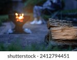 Chopped fire wood logs. Campfire, fire pit filled with burnt wood and flames. A camper sitting in the background.