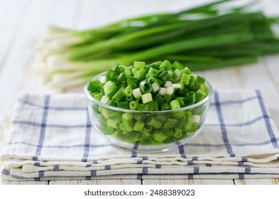 Chopped fresh green onion or scallions in a clear glass bowl , on a white table.