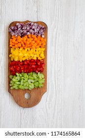 Chopped Fresh Vegetables (carrot, Celery, Red Onion, Colored Peppers) Arranged On Cutting Board On White Wooden Table, Overhead View. Flat Lay, From Above, Top View. Copy Space.