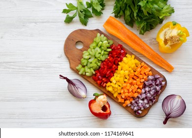 Chopped Fresh Vegetables (carrot, Celery, Onion, Colored Peppers) Arranged On Cutting Board On White Wooden Table, View From Above. Overhead, Top View.