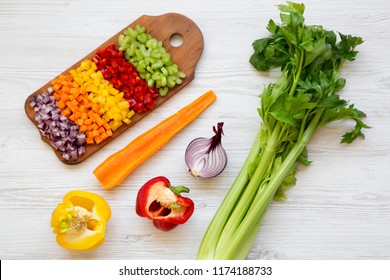 Chopped Fresh Vegetables (carrot, Celery, Red Onion, Red And Yellow Peppers) Arranged On Cutting Board On White Wooden Background, Overhead View. Flat Lay, From Above, Top View.