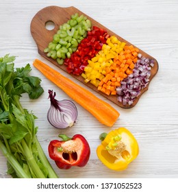 Chopped Fresh Vegetables (carrot, Celery, Red Onion, Red And Yellow Peppers) Arranged On Cutting Board On A White Wooden Surface, View From Above. Flat Lay, Overhead, Top View. 