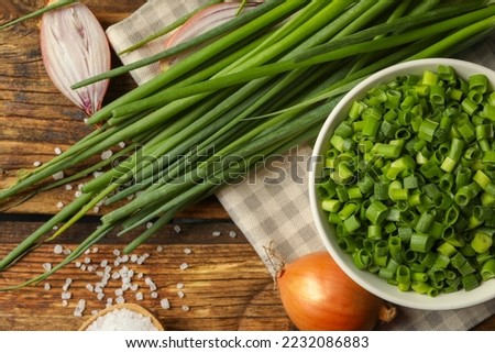 Chopped green onion in bowl on wooden table, flat lay