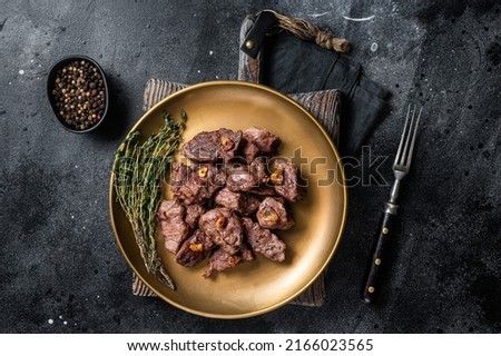 Chopped Grilled Diced Beef garlic steak on a plate with thyme. Black background. Top view