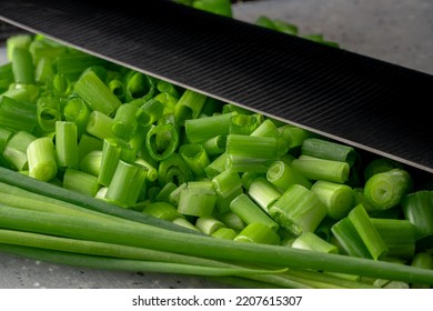 Chopped Pieces And Of Green Onion Stalks. Slices And Stems Of Fresh Green Scallion Next To The Knife Blade. Chopped Shallots Or Chive, Seasonal Greenery, Seasoning For Salad. Macro Shot.