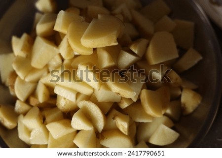 Chopped pieces of potatoes in a steel wok or bowl, under soft light, closeup 