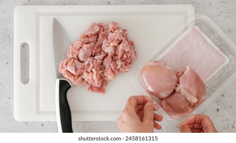 Chopped raw chicken fillet close-up on a white plastic cutting board. The chef cuts meat - Powered by Shutterstock