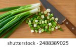 chopped scallions or spring onion on a wooden cutting board, top view. Spring onion and a knife.