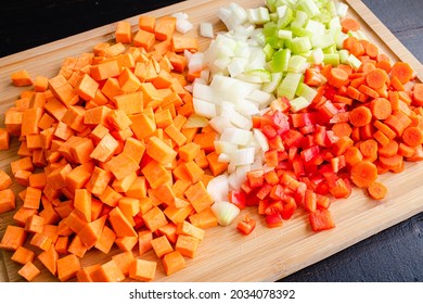 Chopped Vegetables On A Bamboo Cutting Board: Peeled And Diced Sweet Potatoes, Onion, Celery, Carrots, And Red Bell Pepper On A Wood Cutting Board