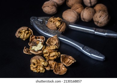 Chopped walnuts on a black background. A steel nutcracker cracks nuts. broken nuts