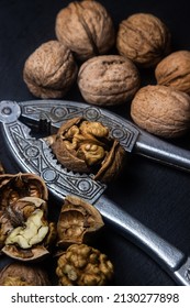 Chopped walnuts on a black background. A steel nutcracker cracks nuts. broken nuts