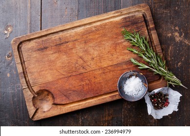 Chopping board, seasonings and rosemary on dark wooden background