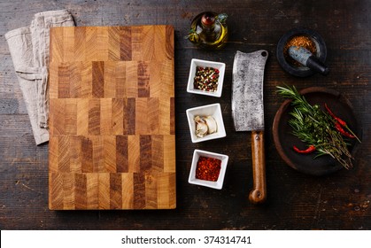 Chopping Cutting Kitchen Board, Seasoning, Herbs And Butcher Meat Cleaver On Dark Wooden Background