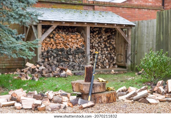 Chopping firewood. Axe and log pile outside a log\
store in a UK garden