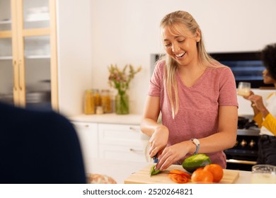 Chopping vegetables, young woman smiling and preparing meal in kitchen with diverse friends. Cooking, happy, together, hobby - Powered by Shutterstock