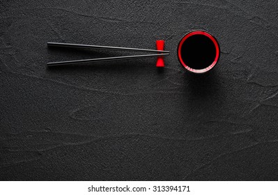 Chopsticks and bowl with soy sauce on black stone background