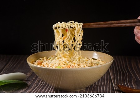 chopsticks with cooked instant noodles on wooden background