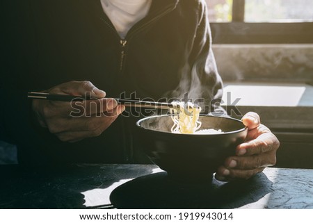 Chopsticks to tasty noodles with steam and smoke in bowl on wooden background, selective focus., Asian meal on a table, junk food concept