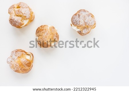 Choux Bun with whipped cream and sugar powder on top on white background. Delicate choux pastry dessert. French cream puff. Top view, copy space