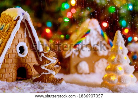 The chrismas tree with light inside on gingerbread houses background.Snowfall. Soft focus.