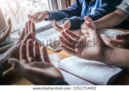 Christian children group praying together around wooden table with open bible page at home, prayer meeting concept.