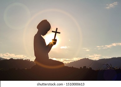 Christian, Christianity, Religion copy space background. Human kneeling down praying and holding christian cross for worshipping God at sunset background.