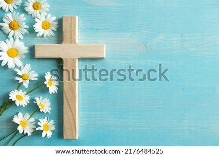 Christian cross and border of white daisy flowers on a blue wood background with copy space 