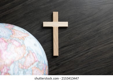 Christian cross on a dark wood background with a partial border of a world globe