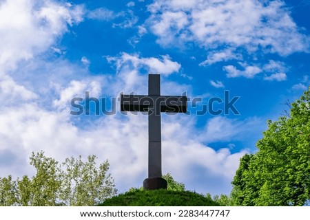 Christian cross on a mound against a blue sky with white clouds. Christian symbol. Religion and culture. Ukrainian Orthodox Church. Catholicism and Protestantism. Place of crucifixion. Easter.