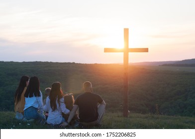 Christian family. Cross. CHRIST IS RISEN.  Happy family on the nature. Easter. Children husband and wife. Wooden cross against the sky. Sunset. Summer