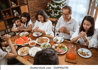 Christian Family Praying Before Meals. Portrait Of People Having Lunch On Christmas Day