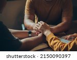 Christian family sitting around a wooden table with open bible page and holding hands to bless and pray for each other. comforting and praying together.Christians and Bible study concept.

 