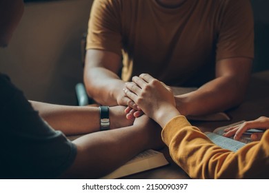 Christian family sitting around a wooden table with open bible page and holding hands to bless and pray for each other. comforting and praying together.Christians and Bible study concept. 