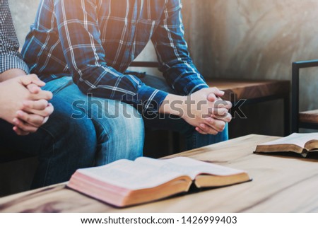 Christian friends sitting on a wooden chair while praying together  with the holy bible on wood table